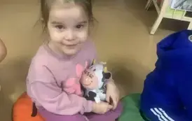 Dziewczynka siedzi na siedzisku i trzyma pluszową książeczkę w kształcie kr&oacute;wki, obok siedzi chłopiec w niebieskim dresie.