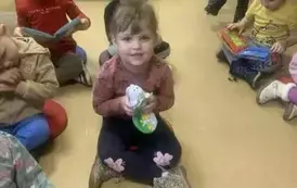 Dzieci siedzą  na siedziskach  w bibliotece i bawią się pluszowymi książeczkami.