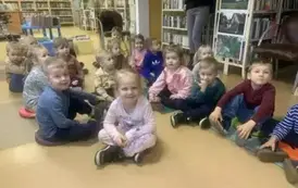 Dzieci siedzą  na siedziskach  w bibliotece.