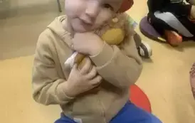 Chłopiec siedzi na siedzisku i przytula do siebie maskotkę. W tle widać innego chłopca.