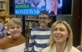 Przy pisarce stoi dw&oacute;ch uśmiechniętych chłopc&oacute;w. Jeden chłopiec ma ubrane okulary.