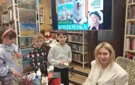 Dw&oacute;ch chłopc&oacute;w i dziewczynka stoją w kolejce do pisarki po zakup książki i autograf.