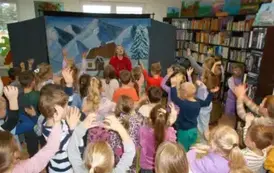 Dzieci stoją obok siebie i podnoszą ręce w g&oacute;rę naśladując Panią przebraną za renifera, kt&oacute;ra stoi z przodu na tle zimowego domu w g&oacute;rach.