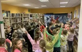 Dzieci gromadnie stoją obok siebie i podnoszą w g&oacute;rę ręce naśladując z przodu Panią przebraną za renifera.