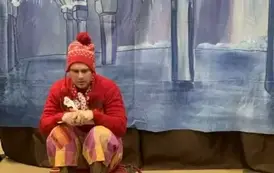 Na tle śnieżnego pałacu siedzi na sankach renifer z notesem. Widać dzieci z publiczności.