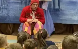 Na tle śnieżnego pałacu siedzi renifer z notesem,a za nim stoi Kr&oacute;lowa Śniegu. Widać dzieci z publiczności.