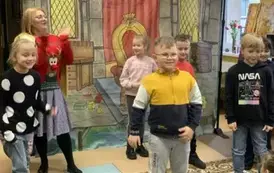 Na tle wnętrza pałacu dzieci z publiczności tańczą razem z kobietą przebraną za renifera, kt&oacute;ra klaszcze w dłonie.