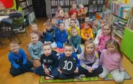 Dzieci siedzą na dywanie i słuchają bajki.