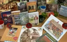 Na biurku wystawione są książki o tematyce kociewskiej, porcelanowe maki i kubki ze wzorem kociewskim.