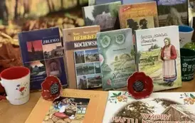 Na biurku wystawione są książki o tematyce kociewskiej, porcelanowe maki i kubek ze wzorem kociewskim.