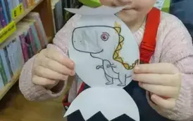 Dziewczynka w jasnych włosach pokazuje swojego pokolorowanego dinozaura.