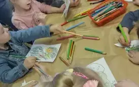 Dzieci przy stole kredkami kolorują dinozaury.