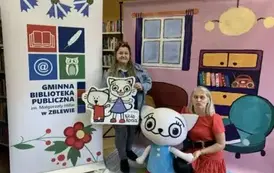 Na tle bajkowego pokoju bohaterka Bajanka trzyma Kicię Kocię za rękę robiąc dziwną minę, a z drugiej strony stoi kierowniczka biblioteki trzyma kartę z podobiznami Kici Koci. Z lewej strony jest logo biblioteki.