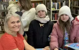 Dwie dziewczynki w białych czapkach stoją przy stoliku pisarki aby zakupić książeczki.