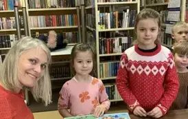 Dwie dziewczynki stoją przy stoliku aby zakupić książeczki od pisarki (Bajanki). Z tyłu widać inne dzieci.