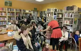 Przy wejściu do biblioteki siedzą rodzice ze swoimi dziećmi. Bajanka podaje jednemu z dzieci czerwony rekwizyt.