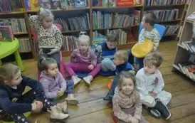Dzieci siedzą na siedziskach w bibliotece i słuchają bajki.