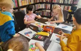 Dzieci przy stole obklejają plasteliną na kartkach kolorowe koguciki.