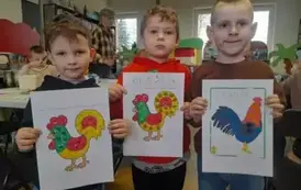 Trzech chłopc&oacute;w pokazuje na kartkach swoje obklejone plasteliną kolorowe koguciki. 