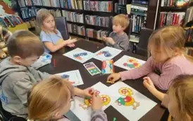 Dzieci przy stole obklejają plasteliną na kartkach kolorowe koguciki.