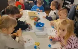 Dzieci siedzą przy białym stole i przyklejają na kartkach brakujące głowy do zwierzątek.