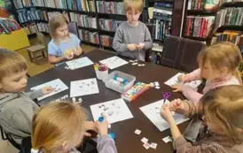 Dzieci przy stole przyklejają na kartkach brakujące głowy do zwierzątek.