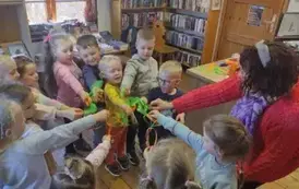 Dzieci stoją z Panią prowadzącą w k&oacute;łeczku i wyciągają jedną rękę do środka ze swoimi zrobionymi marchewkami.