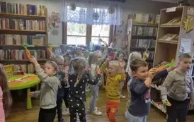 Dzieci trzymając swoje zrobione z papieru marchewki tańczą do piosenki 'Marchewkowe pole"