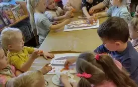 Dzieci podzielone na dwie grupy przy stole ozdabiają stempelkami z marchewki narysowany na dużych kartkach tort.