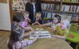 Dzieci przy stole ozdabiają stempelkami z marchewki narysowany na dużej kartce tort.