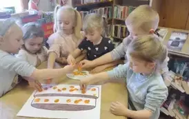 Dzieci przy stole ozdabiają stempelkami z marchewki narysowany na dużej kartce tort.