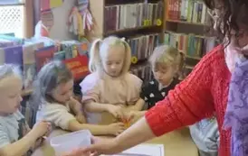 Pani prowadząca podaje dzieciom przy stole stempelki z marchewki, na stole leży narysowany na dużej kartce tort.