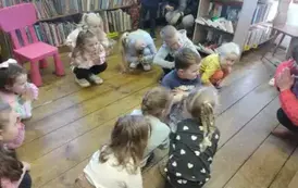 Dzieci kucają na podłodze z rączkami przy sobie naśladując Panią prowadzącą zajęcia.