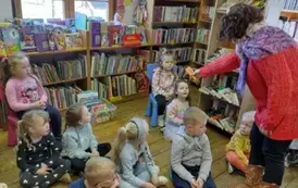 Dzieci siedzą na siedziskach, Pani prowadząca podaje dziewczynce z tyłu dwie marchewki.