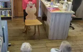 Dzieci siedzą na siedziskach,a z przodu stoi Pani prowadząca, kt&oacute;ra opiera się o drewniane krzesło i opowiada.