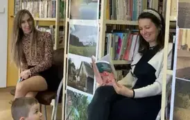 Dwie Panie z przedszkola siedzą z boku na krzesłach, uśmiechają się. Jedna z nich przegląda książkę.