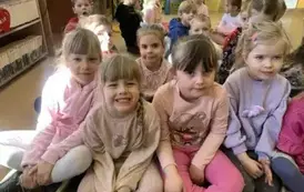 Dzieci siedzą na siedziskach w bibliotece i słuchają bajki