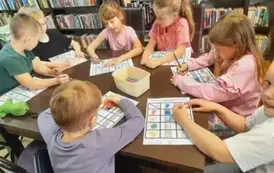 Dzieci przy stole uzupełniają kredkami karty pracy o książce