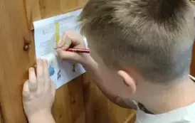 Na drzwiach biblioteki przyklejona jest krzyż&oacute;wka, stoi przed nią chłopiec i wpisuje hasło do krzyż&oacute;wki