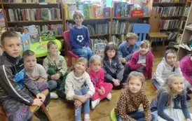 Dzieci siedzą w bibliotece w Borzechowie na siedziskach i krzesłach biorąc udział w zajęciach