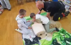 Chłopiec robi sztuczne oddychanie fantomowi, obok jest prezes straży i drugi chłopiec i się przyglądają.