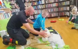 Chlopiec robi uciski na klatce piersiowej fantoma, a obok prezes straży mu pomaga.