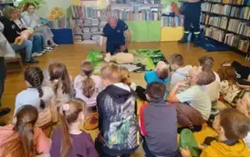 Dzieci siedzą na dywanie, z przodu na drugim dywaniku kuca pochylony nad fantomem przez OSP trzymając rękę na czole fantoma.