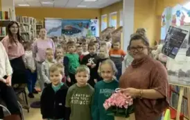 Dzieci wychodzą z biblioteki, troje dzieci wręcza bibliotekarce kwiatek z okazji byłego Święta Bibliotekarza.