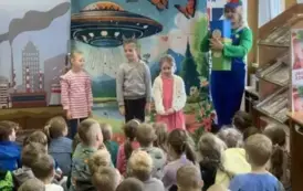 Przed dziećmi stoją na środku trzy dziewczynki i aktorka trzymająca kolorowe kosze do segregacji śmieci.