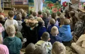 Na dywanie siedzi publiczność dziecięca, a z przodu stoi aktor w przebraniu białego misia z zieloną gałązką w ręku.