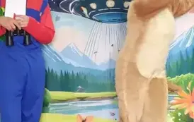 Przed dziećmi stoi aktor przebrany za pieska i trzyma się za glowę, a obok stoi drugi aktor w niebieskim kombinezonie trzymając notes