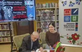 Obok Pana Ćwieka przy stoliku siedzi Czytelniczka czekając na wpis do nowo zakupionej książki.