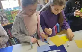 Troje dzieci przy stole wycina kolorowe elementy i przykleja je do kartki.