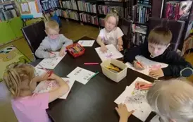 Dzieci przy stole kolorują kredkami na kartkach świnki. Na stole leżą jeszcze karty pracy.